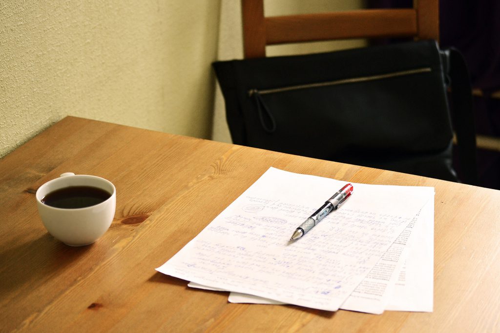 photo of a wooden desk with coffee cup, paper and pen